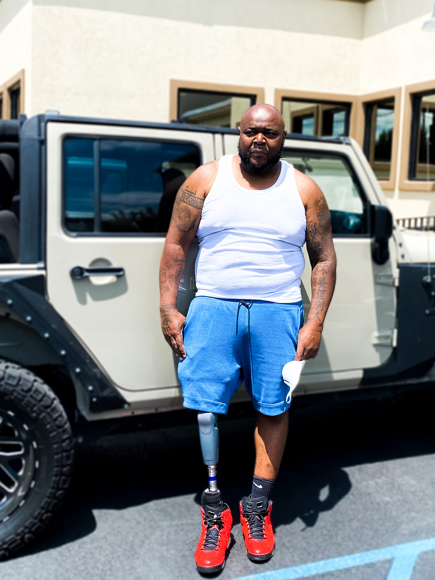 A man with an above knee prosthetic stands confidently outside his car.